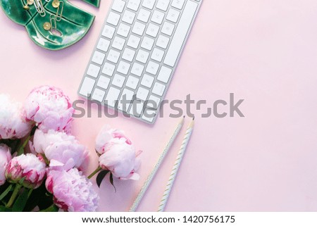 Flat lay home office workspace - modern keyboard with female accessories and peony flowers close up, copy space on pink background