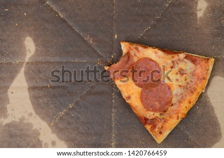 slice of pepperoni pizza with a bite in greasy box