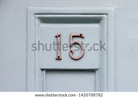 House number fifteen with the 15 on a wooden plaque on a light gray wooden front door
