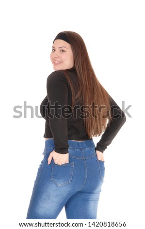 A gorgeous young teen girl standing in jeans and a black sweater 
from the back with her hands in pocket, isolated for white background
