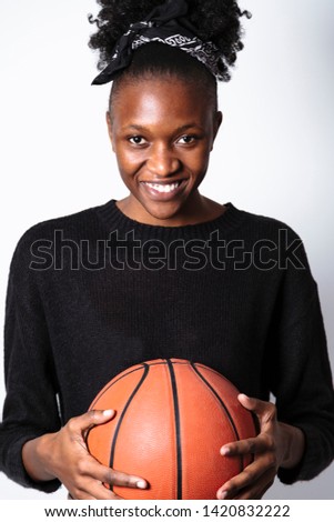 Portrait of Afro-American young relaxed smiling fit woman in black knitted sweater and bandana posing with basketball in hands on white background in studio. Active sports and lifestyle concept