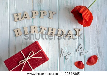 Happy Birthday. Greeting inscription from wooden letters on a light wooden background with a gift, poppy flower and butterflies. Greeting card design with inscription. View from above