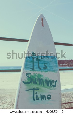 Inscription, It's Summer Time written on a surfboard.