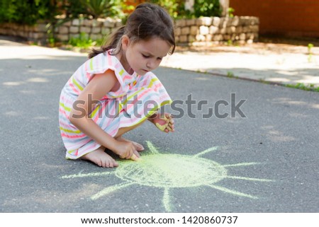 Kids paint outdoors.  Child girl draws with yellow chalk the sun on the pavement (asphalt) on summer sunny day. creative development of children