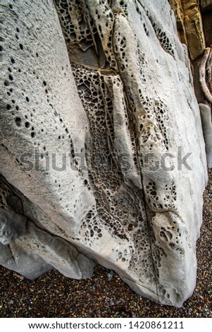 CLOSE UP VIEW OF A LIGHT COLORED SANDSTONE ROCK WITH A SCALE LIKE SURFACE FILLED WITH HOLES COMING TO A POINT ON A PEBBLE SAND BEACH - MOONSTONE BEACH CALIFORNIA