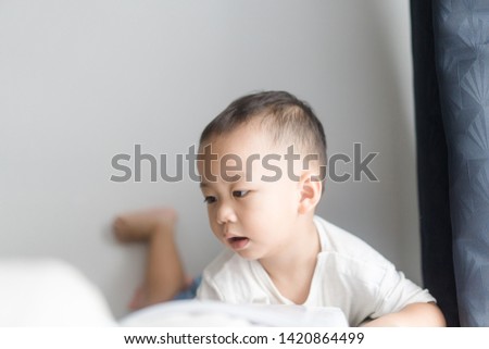2 years little asian toddler boy in white t-shirt reading bible picture story for kid in the morning.Hands holding on a Holy Bible in bed room concept for Education bible study, faith and religion.