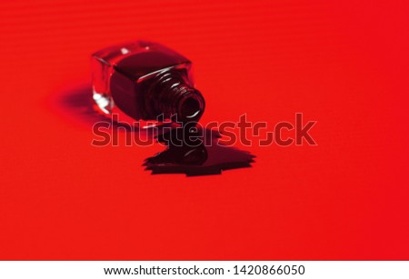 Dark nail polish spilled from the bottle. Vibrant bright red background.