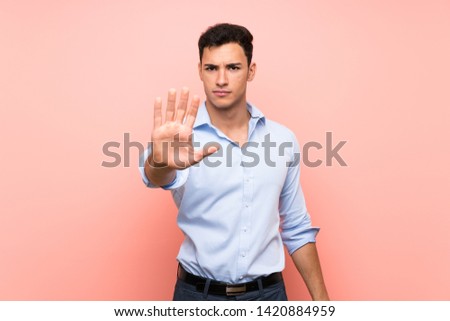 Handsome man over pink background making stop gesture