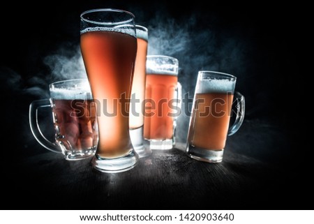 Creative concept. Beer glasses on wooden table at dark toned foggy background. Selective focus