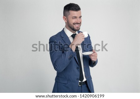 A businessman with a stylish hairstyle and beard keeps a cup of coffee and smiles, looks to the side where there is a free space for your logo or text. Isolated on a white background