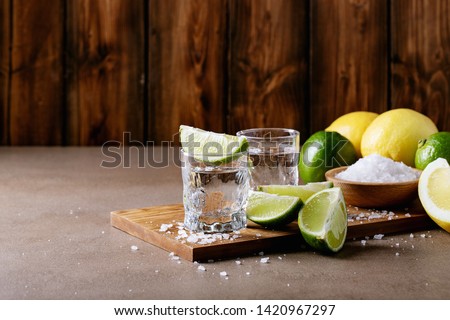 Tequila in a glass served with lemons, limes and salt over brown texture background Royalty-Free Stock Photo #1420967297