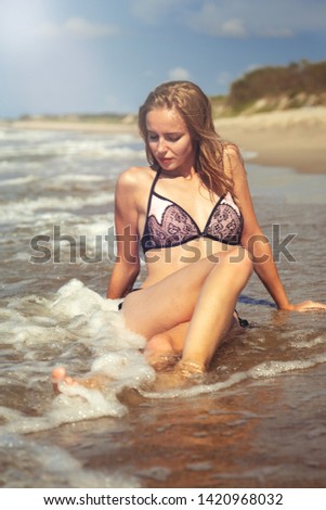 young blond woman in swimsuit at sea surf with foam sitting under sun rays