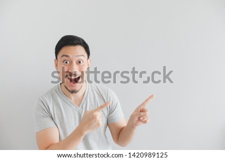 Wow and surprised face of Asian man in grey t-shirt with hand point on empty space.