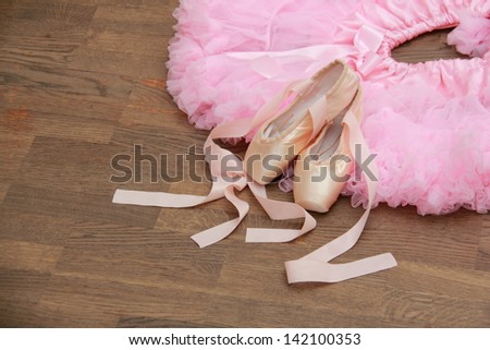 Beautiful pink tutu and pointes with ribbons lie on a dark wooden floor in the ballet hall
