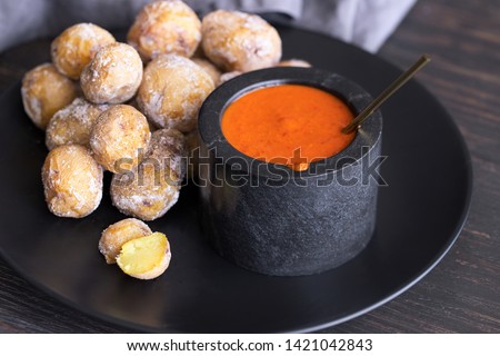 Famous Canary Islands dish, Papas Arrugadas (wrinkly potatoes with salt) and Mojo picon (red sauce) on wood table Royalty-Free Stock Photo #1421042843