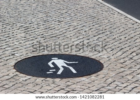 White pedestrian sign on cobblestone pavement