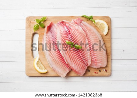 Raw fish fillet of tilapia on a cutting Board with lemon and spices. White table with copy space Royalty-Free Stock Photo #1421082368