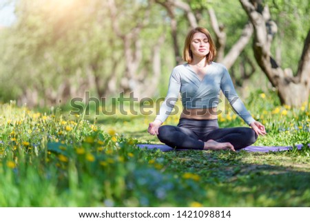Picture of woman doing yoga sitting in lotus position on blue rug in woods