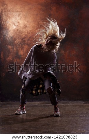 Photo of young blonde dancer woman in torn jeans and sneakers on dark brown background