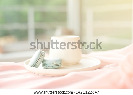 French blue macaroon and coffee cup standing on a wooden table with a pink tablecloth white vase with flowers roses and greens.