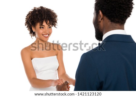 selective focus of happy african american bride looking at bridegroom while holding hands isolated on white 