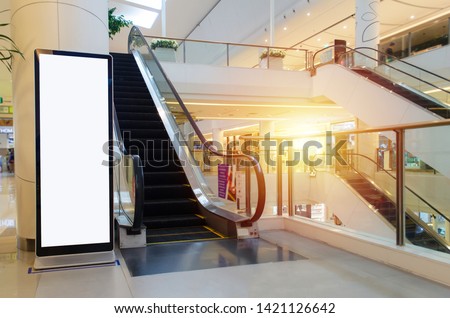 blank showcase billboard or advertising light box for your text message or media content with escalator in modern department store shopping mall, shopping center, commercial and marketing concept Royalty-Free Stock Photo #1421126642