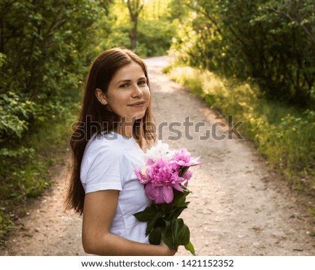 Beautiful girl in a white T-shirt with peonies in their hands against the background of road in the forest