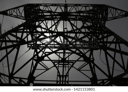 Outdoor view from bellow of an electrical pylon with iron cables and metallic bars. Silhouette of a steel construction with a grey white sky in background. Symbol picture of electricity distribution.