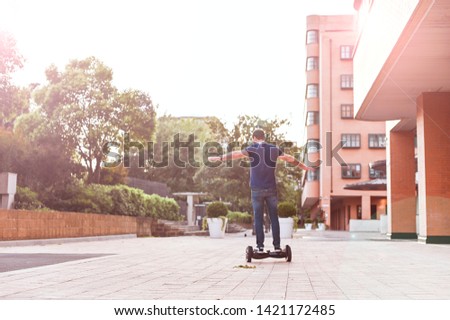 A man in jeans and sneakers with a hoverboard in the city. Happy boy riding around at sunset. Modern electronics for relaxation and entertainment. Sun glare on the photo.