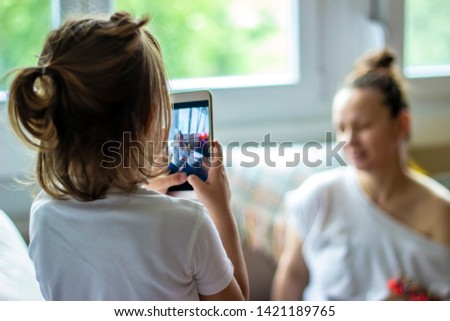 Beautiful little girl taking pictures of her mother with the smart phone. Young woman enjoying with her daughter. Happy mother with a child take pictures on mobile.