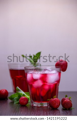 In two glasses poured a red cocktail with ice, next is ripe strawberries and a branch of mint.