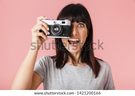 Image of a beautiful amazing excited happy woman photographer posing isolated over light pink background wall holding camera.