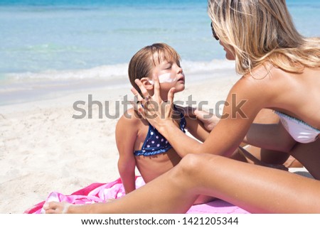 Beautiful family visiting sunny beach, mother applying uva sun protection cream on child face, covering skin, outdoors. Nordic mom and child tourists on summer vacation, leisure recreation lifestyle.