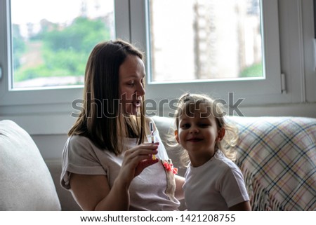 Mother is hollding syringe in front of her daughter. Women sitting on couch and showing her daughter medication she is about to take. Concept of health life.  