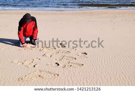 man sit and drawing many heart on sandy beach