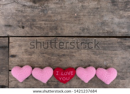 Pink knitting hearts arrange in the row with  red "I Love You" heart on the center on the wooden rough table. Copy space for editing and text.