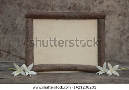 Brown wooden frame on the rough wooden table with the white millingonia. Background of the rock wall. Sun light shines on the frame. Copy space for edting and text.