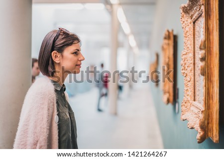 Beautiful female in gallery museum looking at art. Side view of young caucasian woman standing in an art gallery in front of framed paintings displayed on a wall Royalty-Free Stock Photo #1421264267