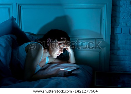 Young attractive woman awake late at night using smart phone lying in bed in a dark bedroom. Using mobile for chatting and sending messages in internet addiction, mobile abuse and insomnia concept Royalty-Free Stock Photo #1421279684