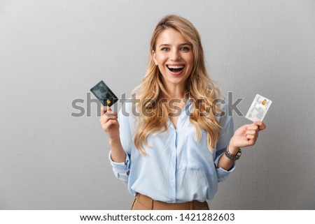Image of a happy young pretty blonde business woman posing isolated grey wall background holding two credit cards.