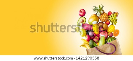 Colorful yellow panorama banner with copy space of a large assortment of fresh tropical fruit and juices rich in vitamins spilling from a reusable grocery bag in a healthy diet concept