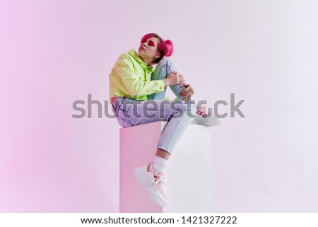 woman with pink hair in stylish clothes sits on a cube