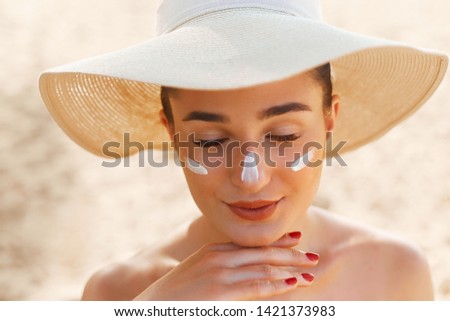 Skin care. Beauty Concept. Young pretty woman applying sun cream and touch own face. Female in hat smear sunscreen lotion on skin. Skin Protection and dermatology.