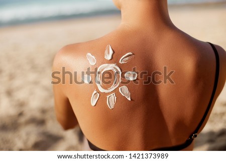 Woman Applying Sun Cream on Tanned  Shoulder In Form Of The Sun. Sun Protection.Sun Cream. Skin and Body Care. Girl Using Sunscreen to Skin. Female Holding Suntan Lotion and Moisturizing Sunblock. Royalty-Free Stock Photo #1421373989