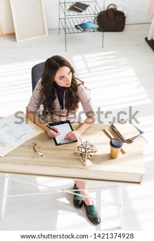 overhead view of pensive girl holding pen near clipboard