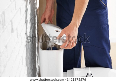 Plumber repairing toilet tank in restroom