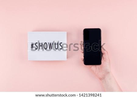 Creative top view flat lay of lightbox with hashtag Show Us message and mobile phone in hand mockup pink background minimal style. Concept Project world largest stock photo collection created by women