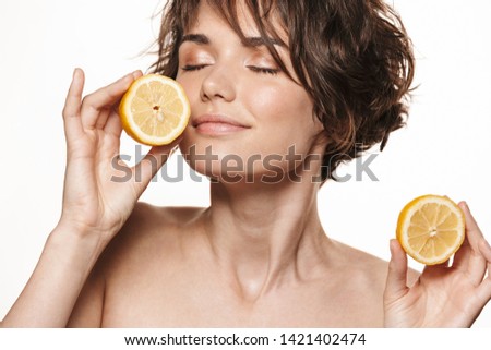 Beauty portrait of an attractive young shirtless brunette girl standing isolated over white background, showing sliced lemon
