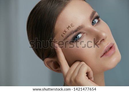 Beauty makeup. Woman face with messy eyebrow and fix me sign on skin closeup. Girl model with bushy fluffy messed up eyebrows and words written above. Eyebrow correction concept Royalty-Free Stock Photo #1421477654
