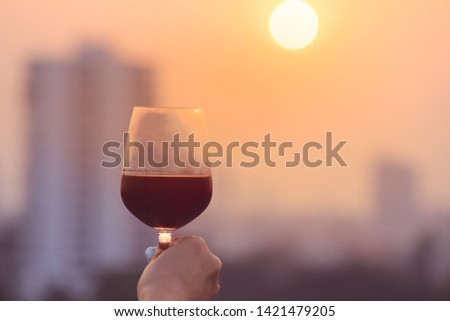 Woman’s hand holding red wine glasses on balcony during sunset, celebration concept